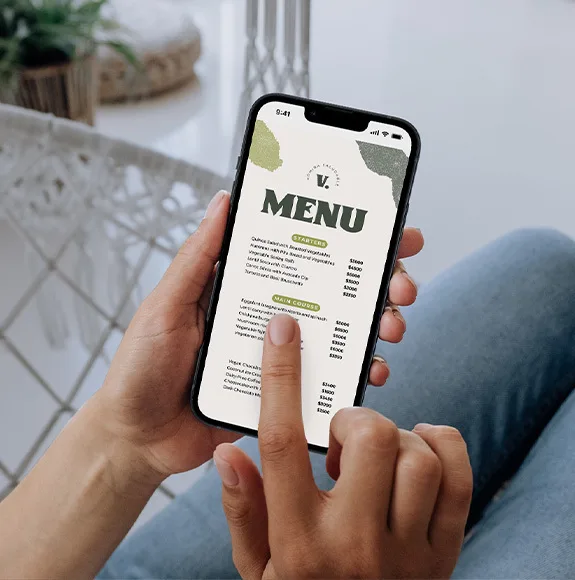 Osoba drží smartphone s otevřeným digitálním menu a prstem prochází nabídku jídel.