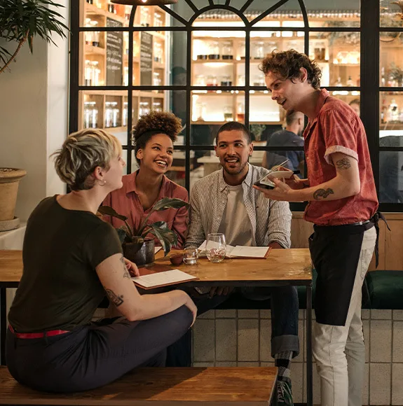 Číšník přijímá objednávku od skupiny mladých lidí v moderní restauraci.