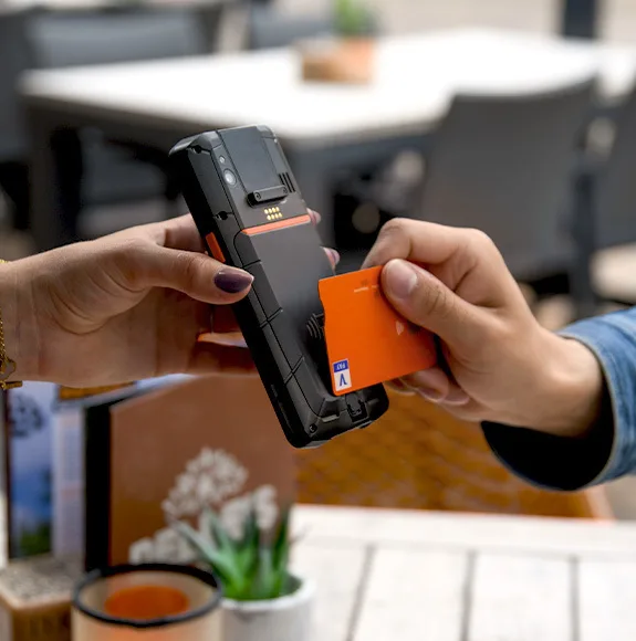 Close-up of a contactless payment: Person holds an orange credit card to a payment terminal.