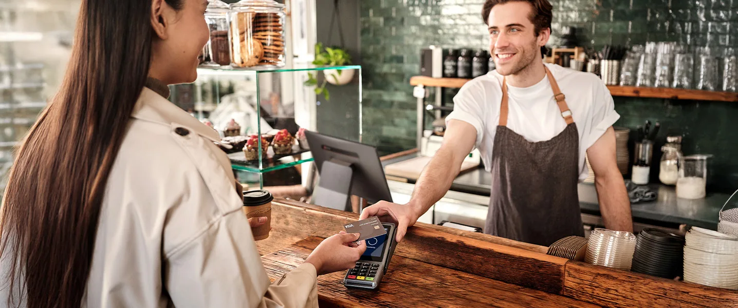 A barista hands a customer at the café counter a payment terminal where she pays with a Visa credit card.