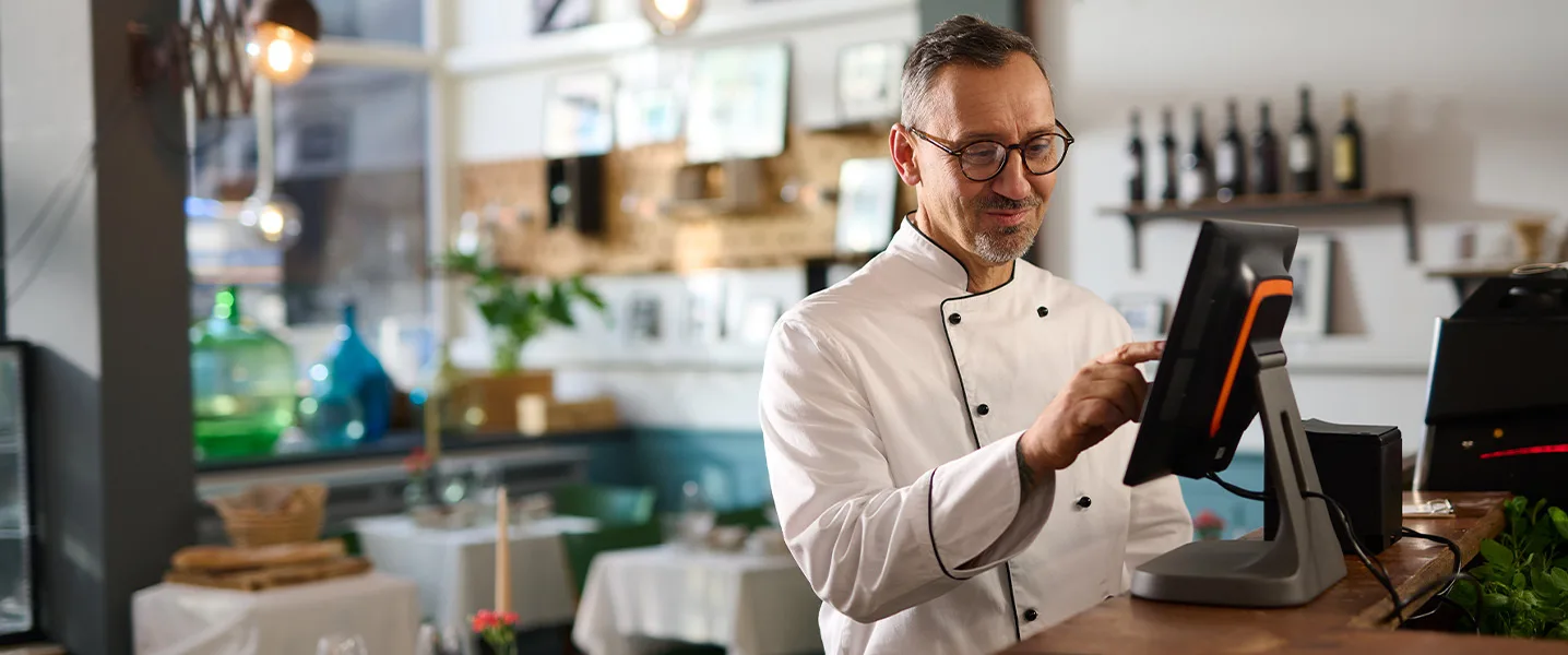 Chef in white uniform operates a touchscreen POS system in a restaurant.