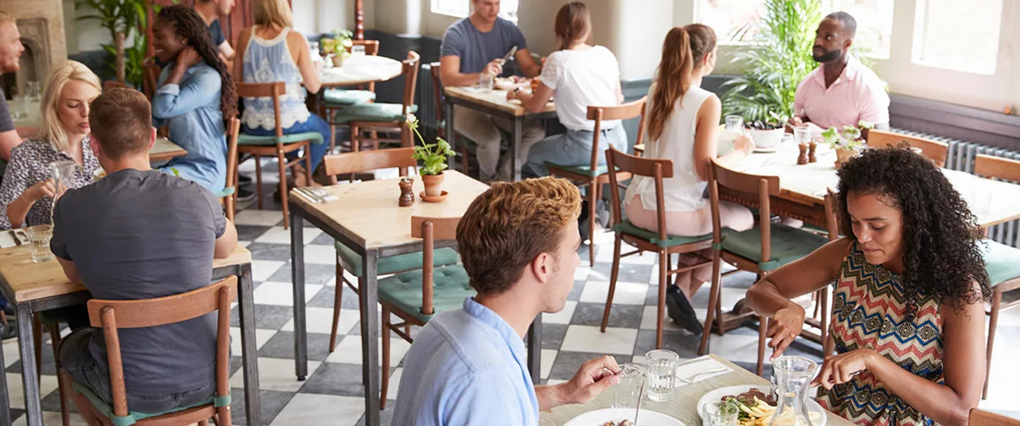 Guests sit in a cozy restaurant and enjoy their meal at wooden tables in daylight.