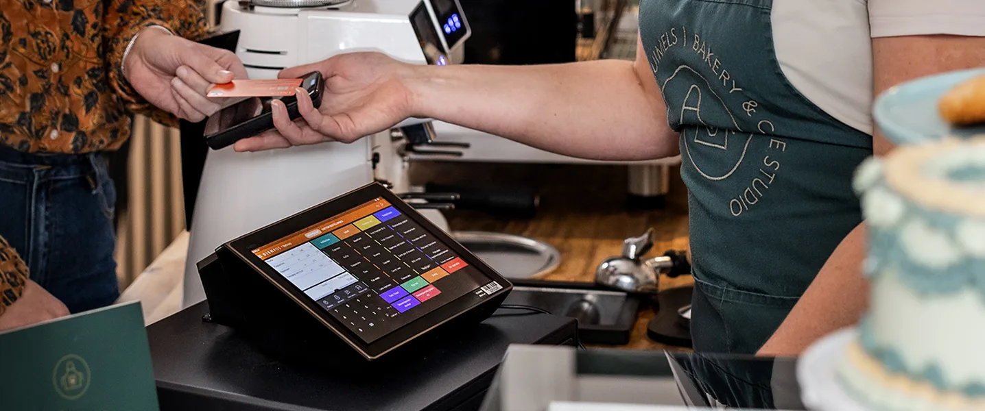 A man is making a contactless payment with a debit card on a mobile terminal held by a waiter above the touch screen of a digital POS system.
