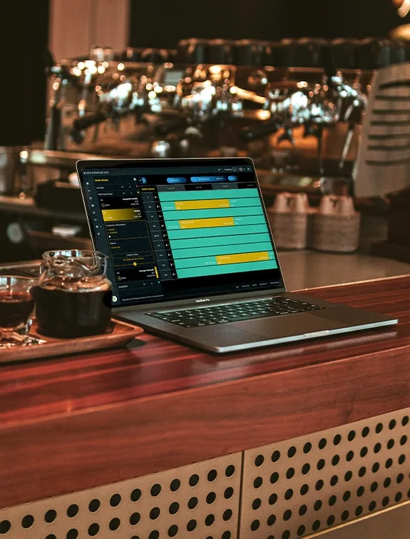 Laptop at the bar shows a digital reservation system next to a pot of coffee.
