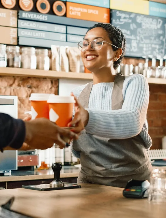 Café employee hands a guest two coffee cups over the counter.