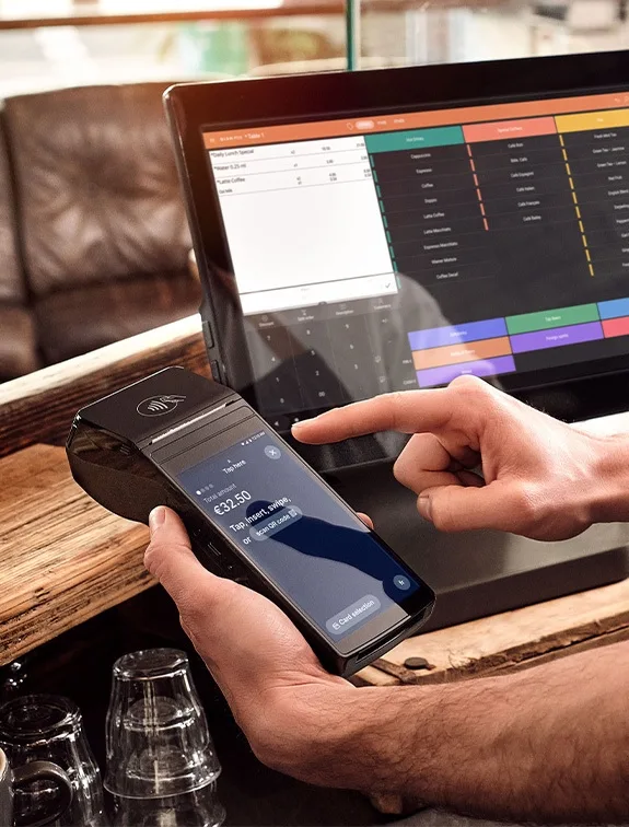 Close-up of a modern card reader displaying an amount, waiter confirms payment on screen.