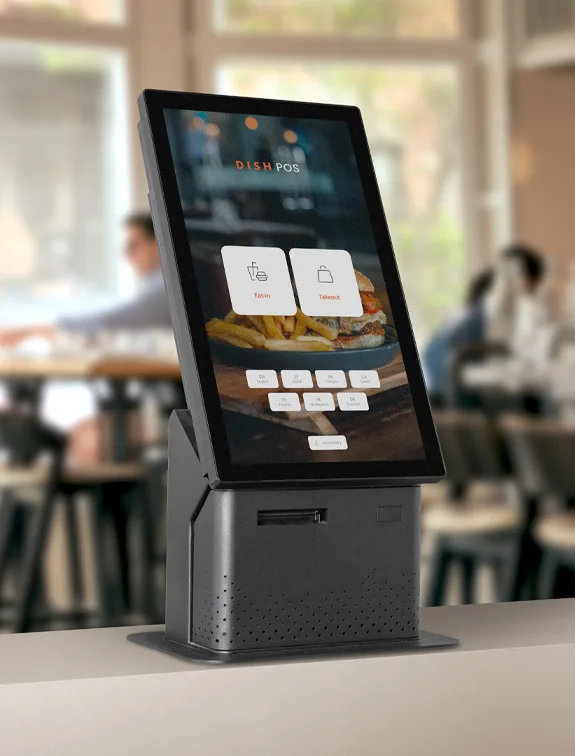 A self standing order kiosk with a turned on touch display screen is showing a menu