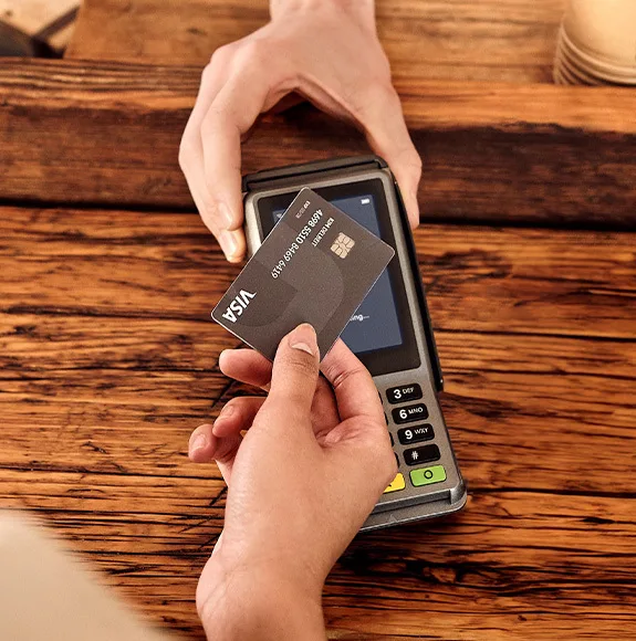 Close-up: Person holds a black card to a payment terminal on a wooden table surface.