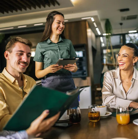 Une serveuse amicale prend la commande de deux clients dans le restaurant à l'aide d'une tablette.