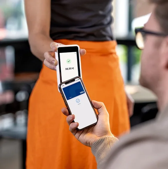 Un client tient un smartphone avec une carte Visa numérique devant un lecteur de carte mobile, un paiement sans contact réussi est affiché.