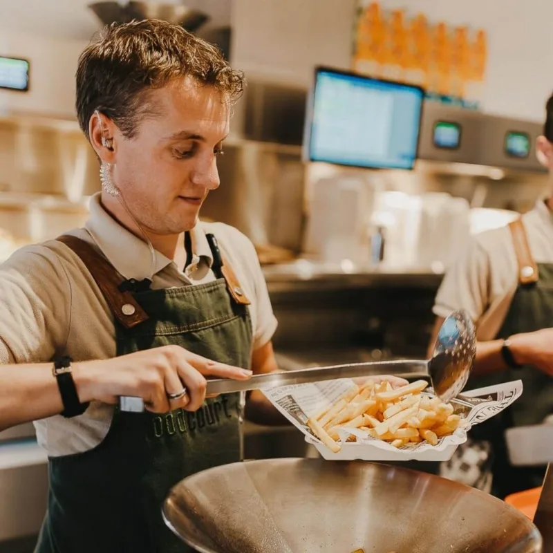Restaurantmitarbeiter, der frisch zubereitete Pommes frites in einer Bar-Küche serviert.