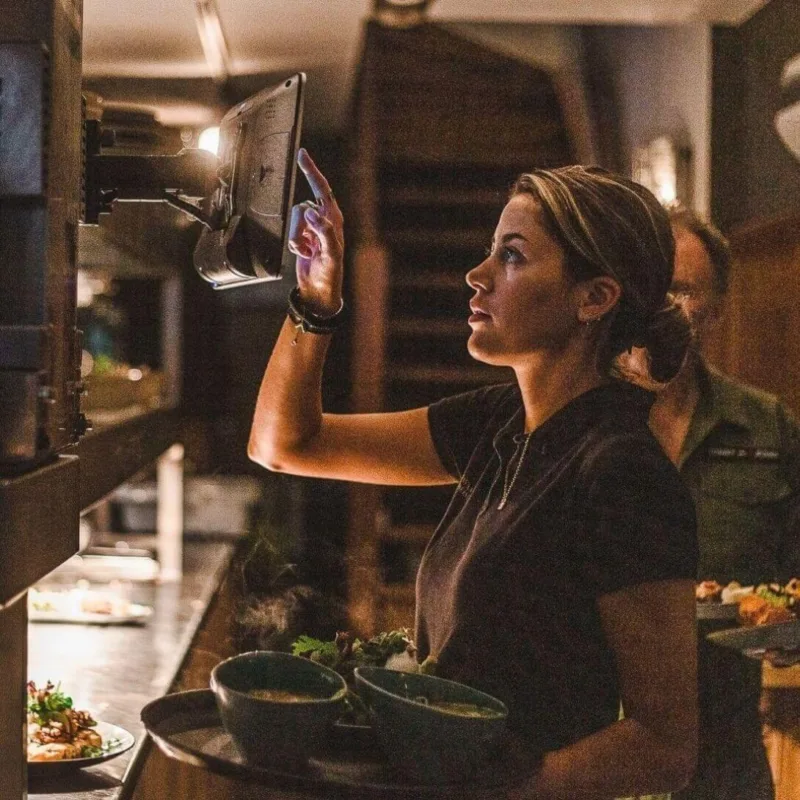 Restaurantmitarbeiter, der eine Küchenanzeigetafel nutzt, während er fertige Gerichte transportiert.