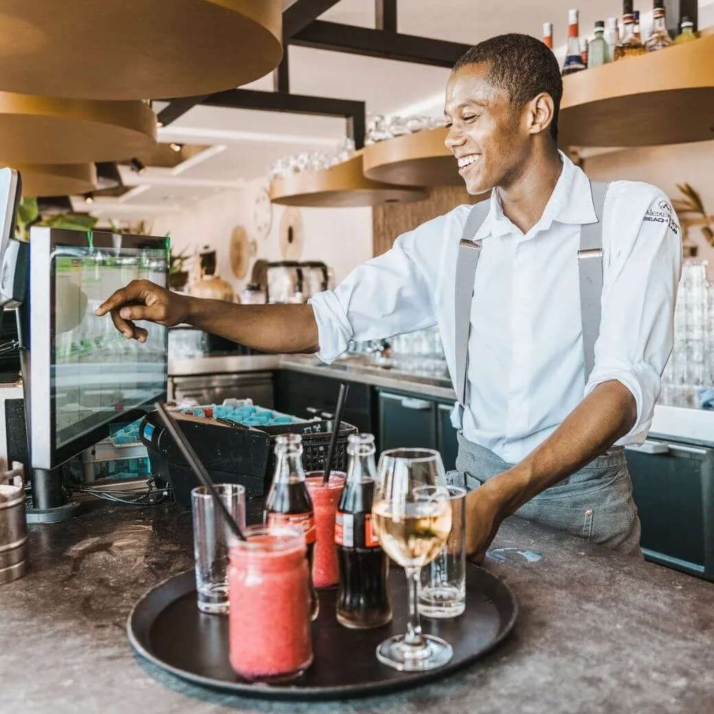 Restaurantmitarbeiter, der ein Touchscreen-Kassensystem bedient, während er Getränke für den Service zubereitet.