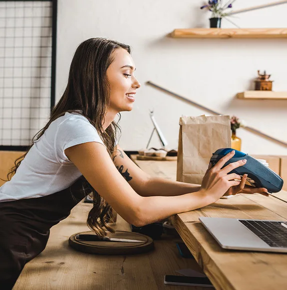 Café-Mitarbeiterin hält ein Bezahlterminal über den Tresen, um eine Zahlung entgegenzunehmen.