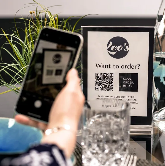 Un cliente scansiona un codice QR su un display con le parole "Vuoi ordinare? Scansiona, ordina, rilassati!" utilizzando il proprio smartphone.