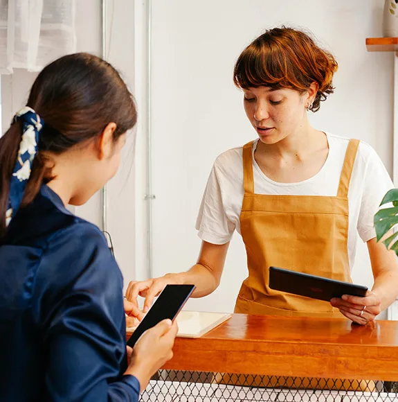 Dipendente del caffè con grembiule marrone al bancone controlla la prenotazione di un cliente con uno smartphone.