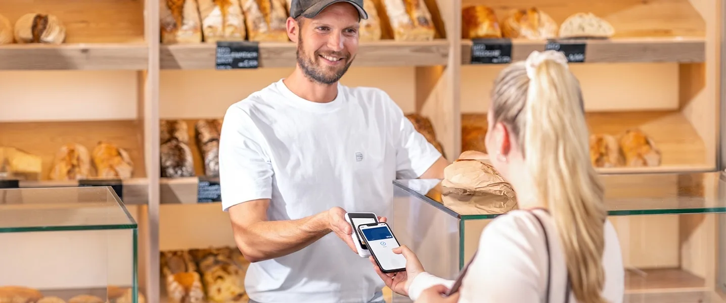 Il cliente paga senza contatto con lo smartphone in una panetteria, il venditore gli porge il terminale di pagamento.