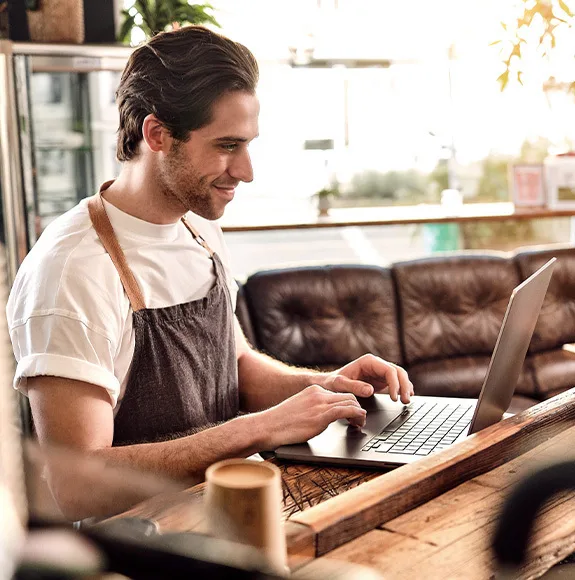 Il cameriere lavora su un laptop al bar e sorride.