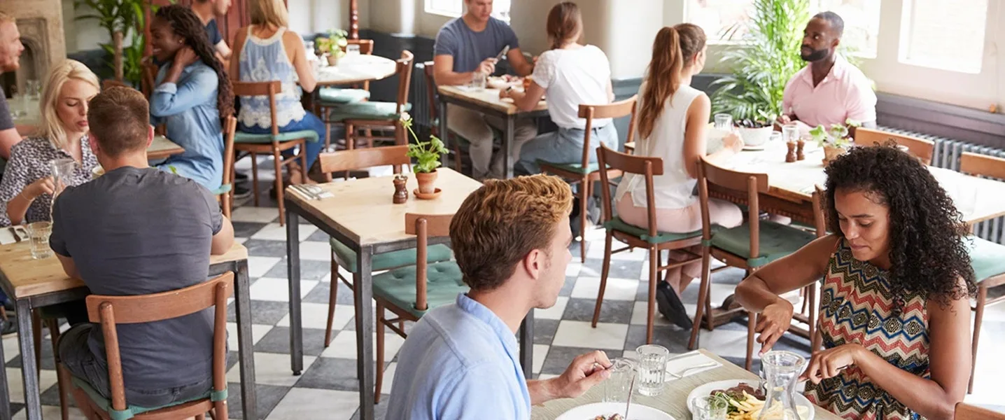 Goście siedzą w przytulnej restauracji i delektują się posiłkiem przy drewnianych stołach w świetle dziennym.