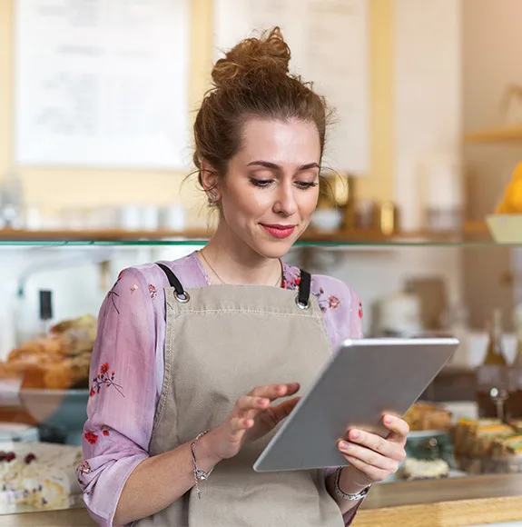 Um barista usa um avental e olha atentamente para um tablet para gerir encomendas ou menus digitais.