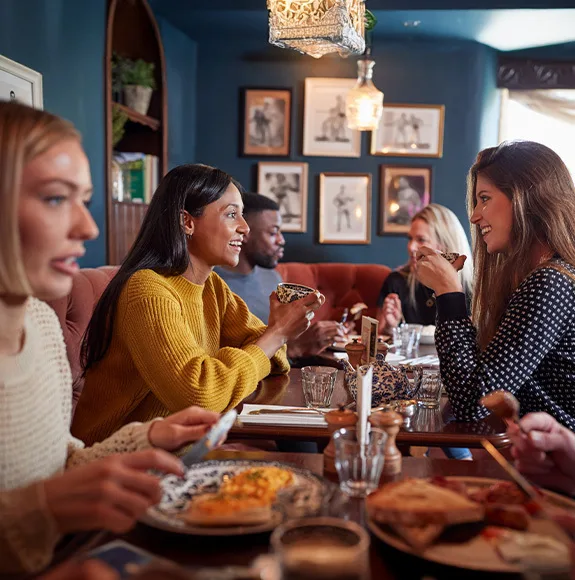 Grupo de amigos sentados en un restaurante, riendo y charlando mientras disfrutan de comida y bebidas.