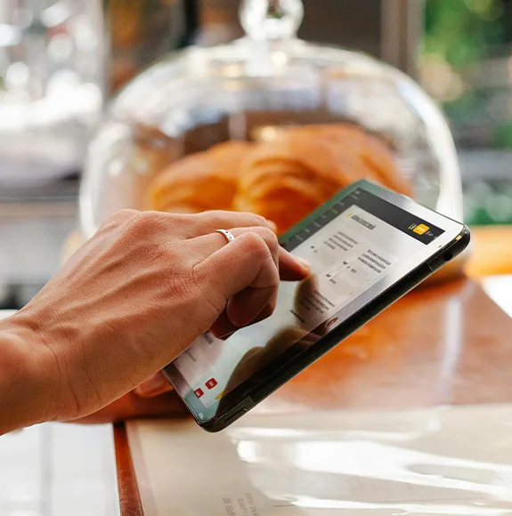 Mano opera una tableta con una plantilla de sitio web abierta, croissants al fondo.