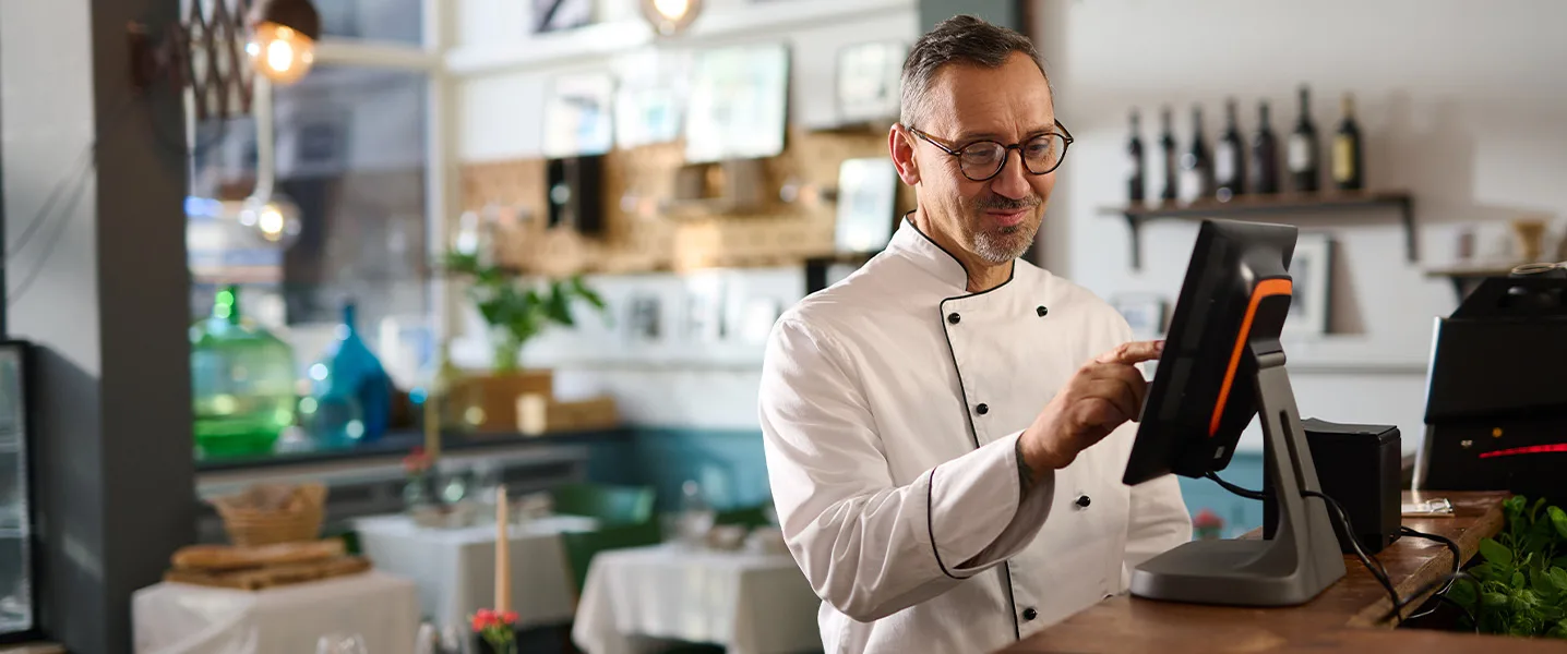 Beyaz üniformalı şef, bir restoranda dokunmatik ekranlı POS sistemini kullanıyor.