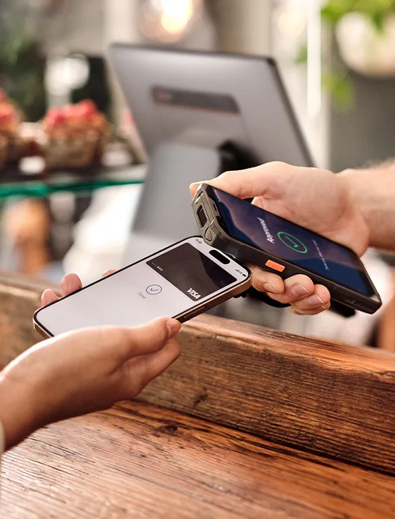 La mano de una persona sostiene un teléfono en el que se ve una tarjeta de crédito digital en la pantalla, y lo acerca a un dispositivo de pago sin contacto de DISH POS que sostiene el camarero.
